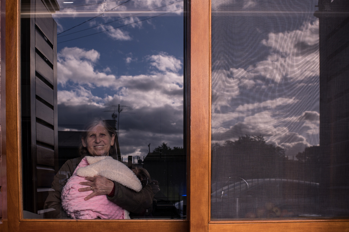 Batizado em São José do Sul, avó com o bebê no colo através da janela de casa