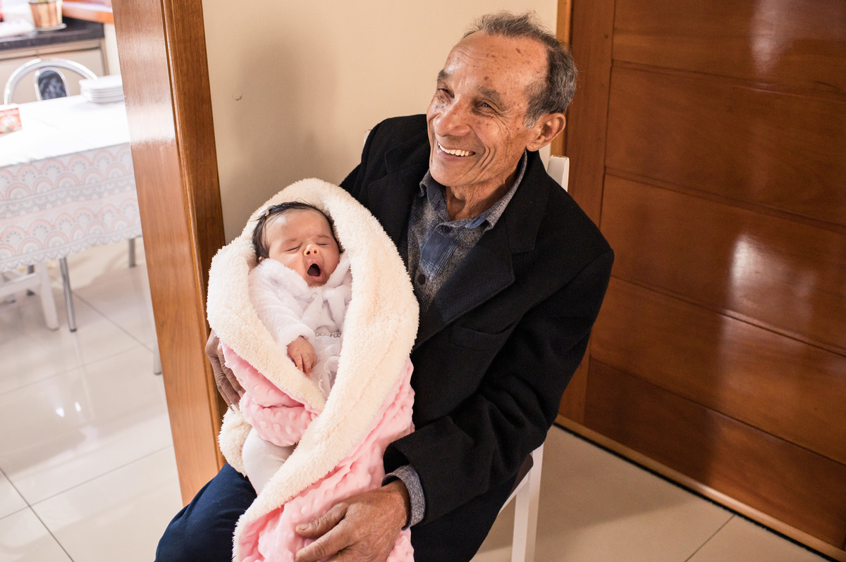 Batizado em São José do Sul, bebê no colo do avô dentro de casa