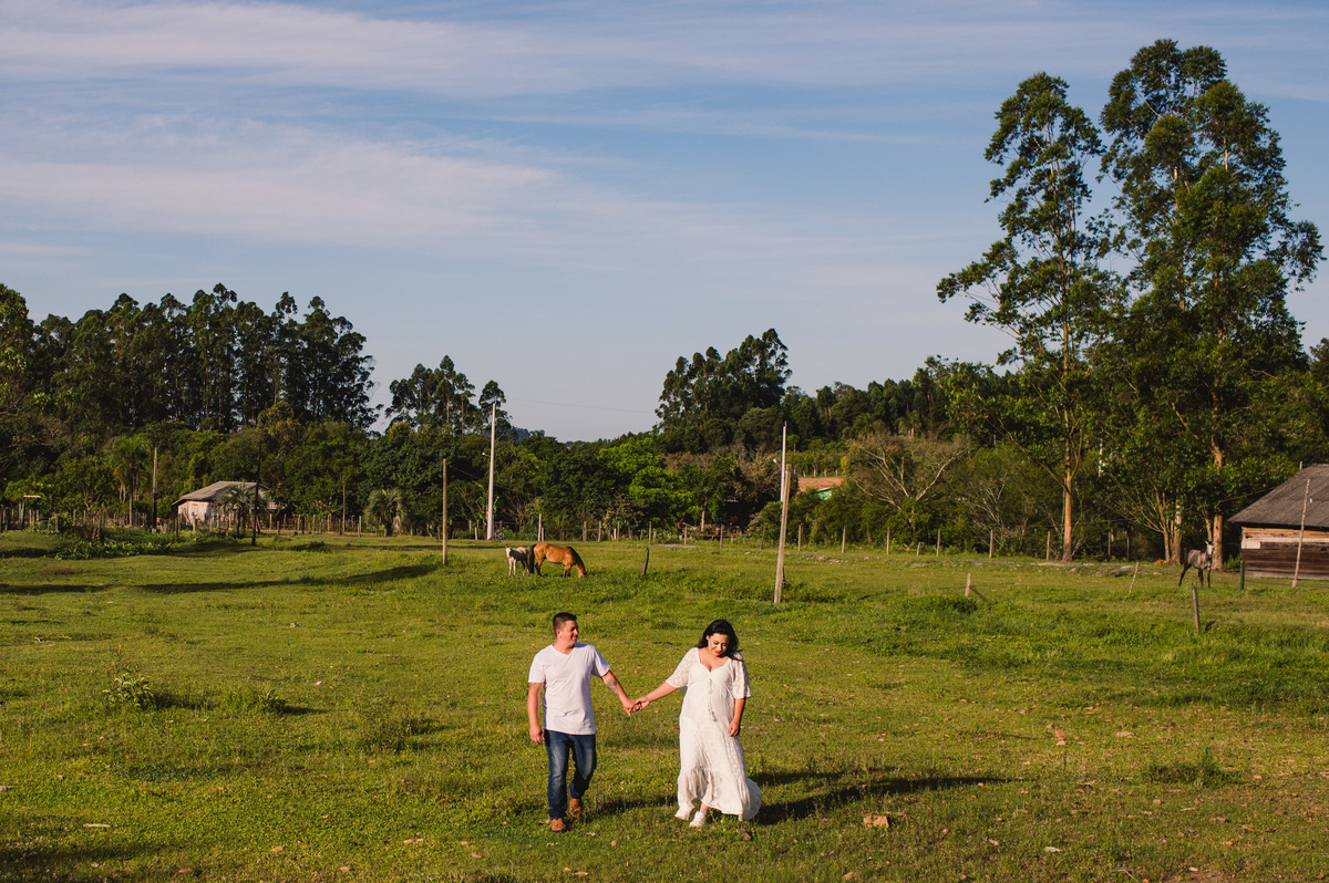 Ensaio gestante na chácara, casal caminhando pelo campo, céu bonito