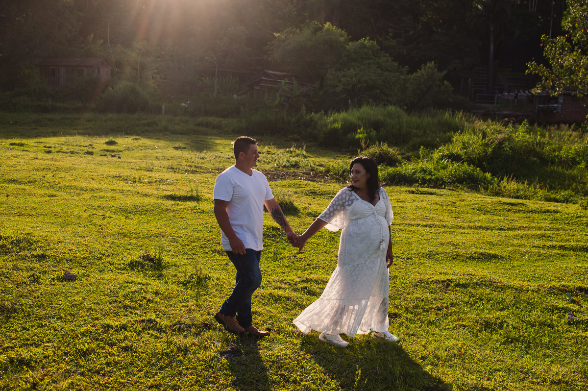 Ensaio gestante na chácara, casal caminhando no campo, luz bonita do final da tarde