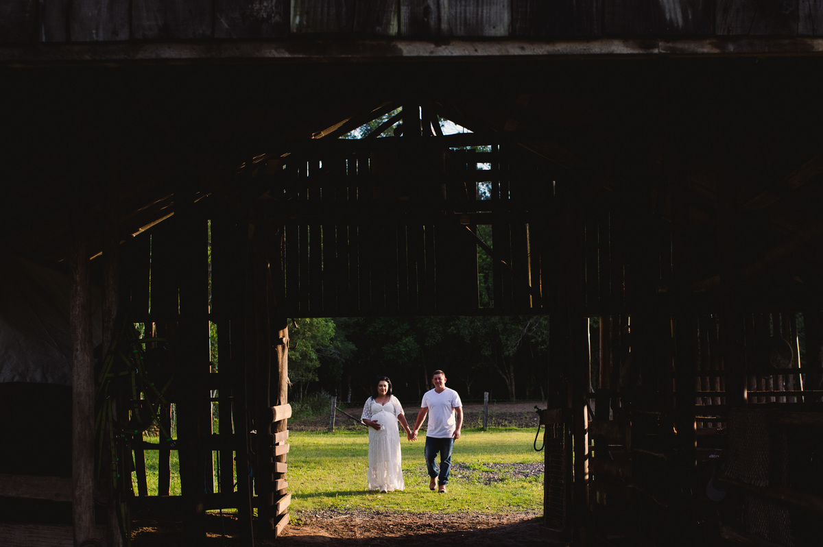 Ensaio gestante na chácara, casal visto através da porta de galpão