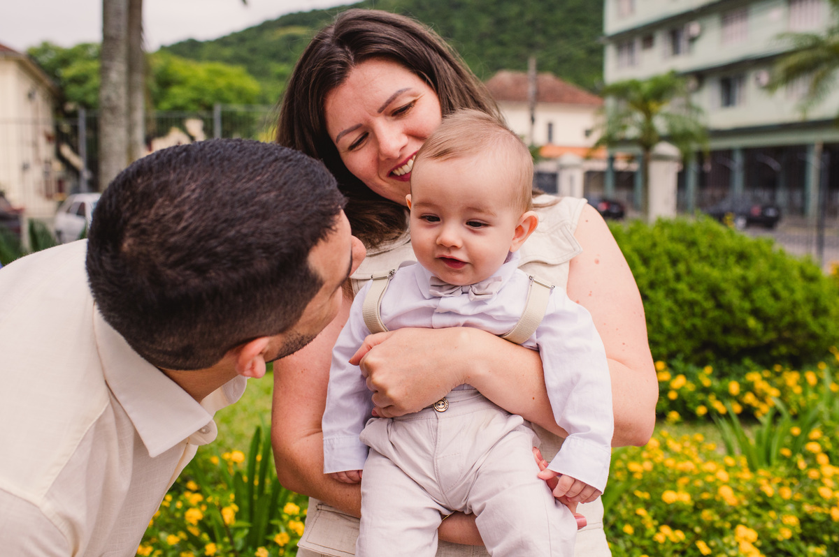 Fotos de batismo na Catedral de Montenegro - Fotógrafa Claudia Wallauer - criança no colo dos pais em frente à Catedral
