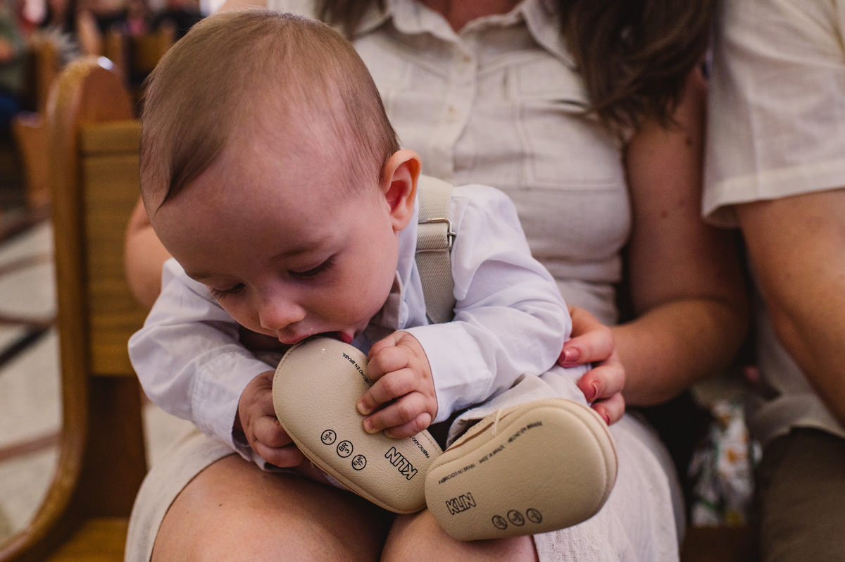 Fotos de batismo na Catedral de Montenegro - Fotógrafa Claudia Wallauer - criança mordendo o sapato no próprio pé
