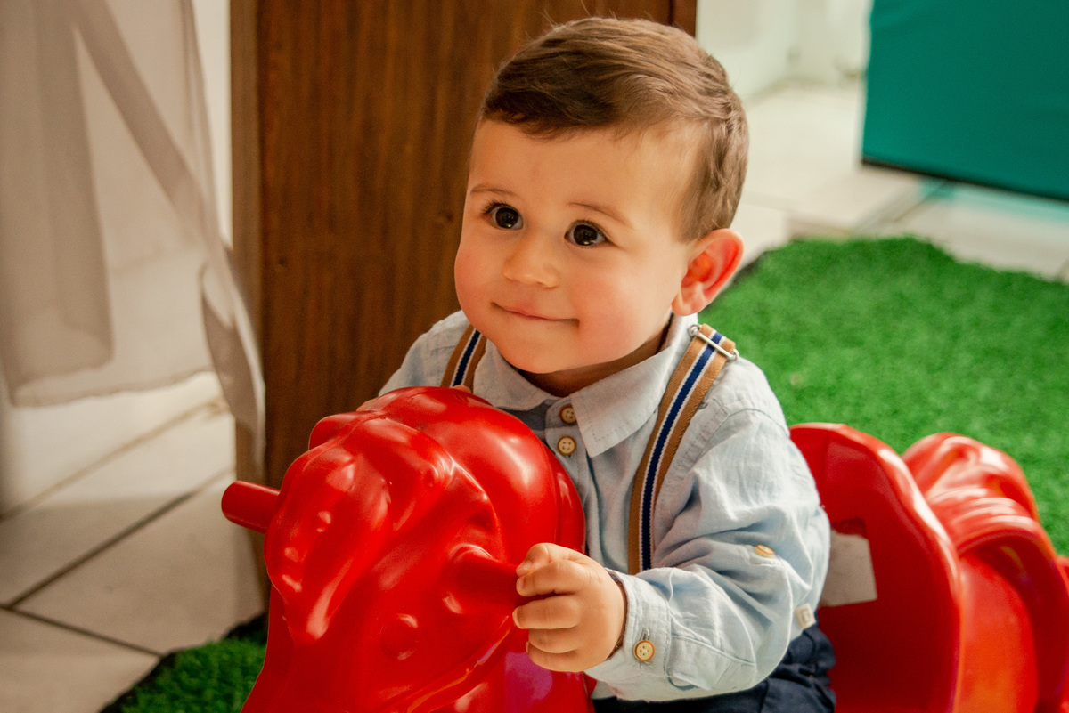 Festa de aniversário de um aninho, menino brincando num cavalinho, carinha sapeca