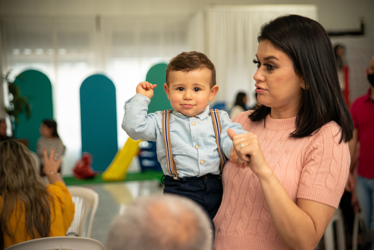 Menino de um aninho em sua festa de aniversário no colo da mãe imitando o acelerador de uma moto