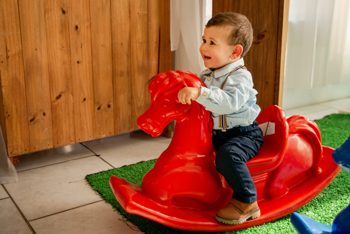 Festa de aniversário de um aninho, menino brincando num cavalinho, sorrindo
