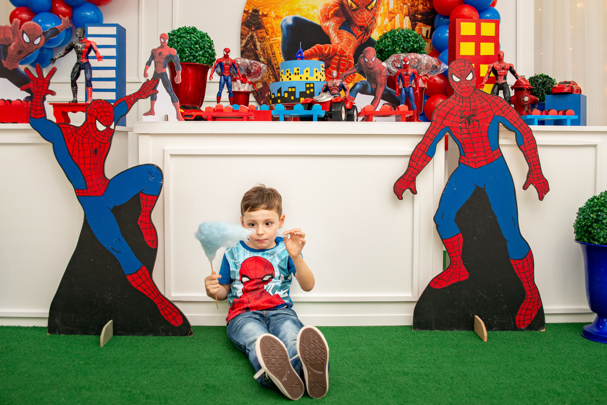 menino comendo algodão doce em frente à decoração de festa infantil do homem 