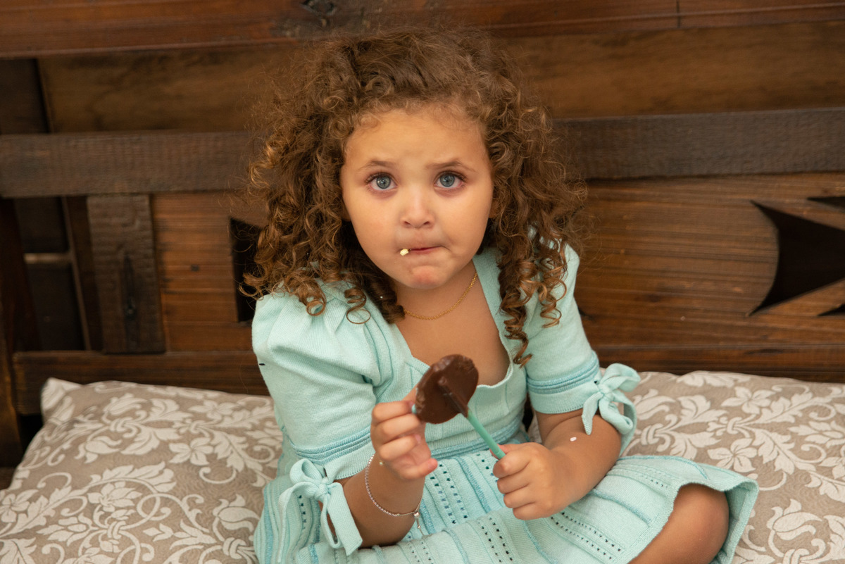 menina comendo doce de chocolate com expressão espontânea em casa de festa infantil em Montenegro RS