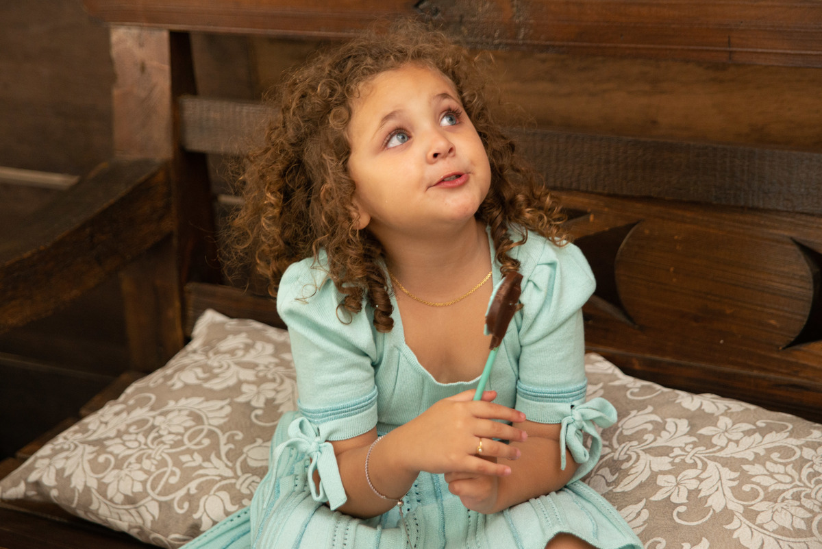 menina comendo doce de chocolate com expressão espontânea em casa de festa infantil em Montenegro RS