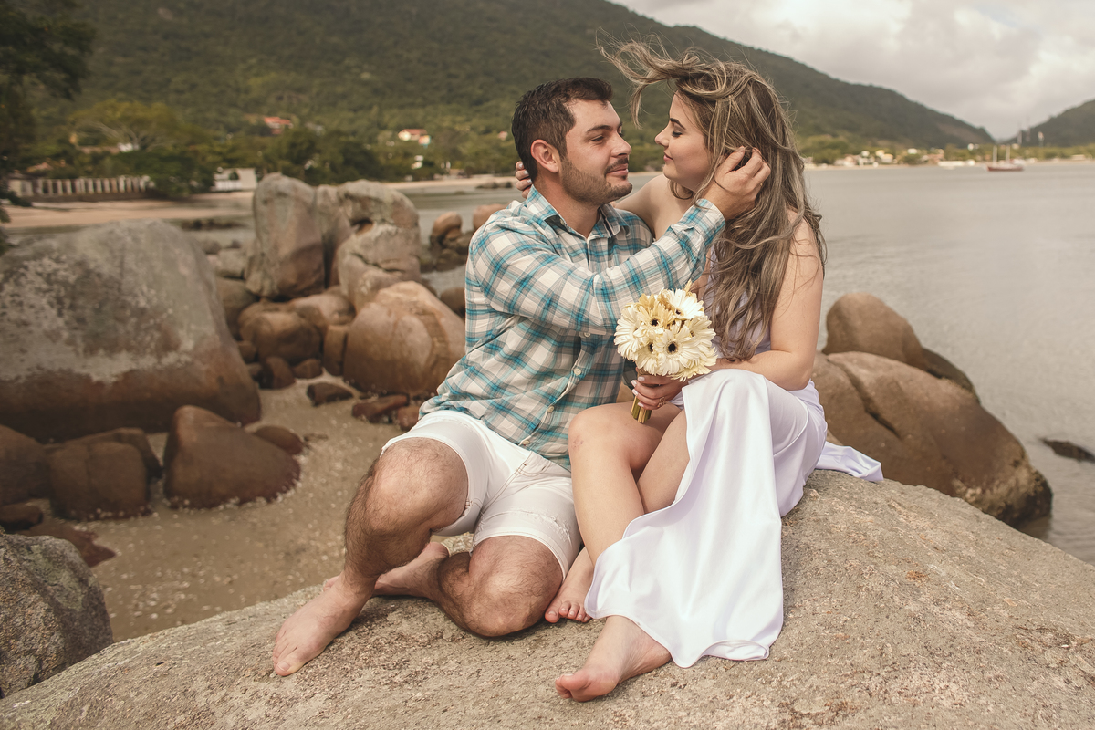Ensaio pré wedding com noivos sentados sobre pedra na praia de Florianópolis