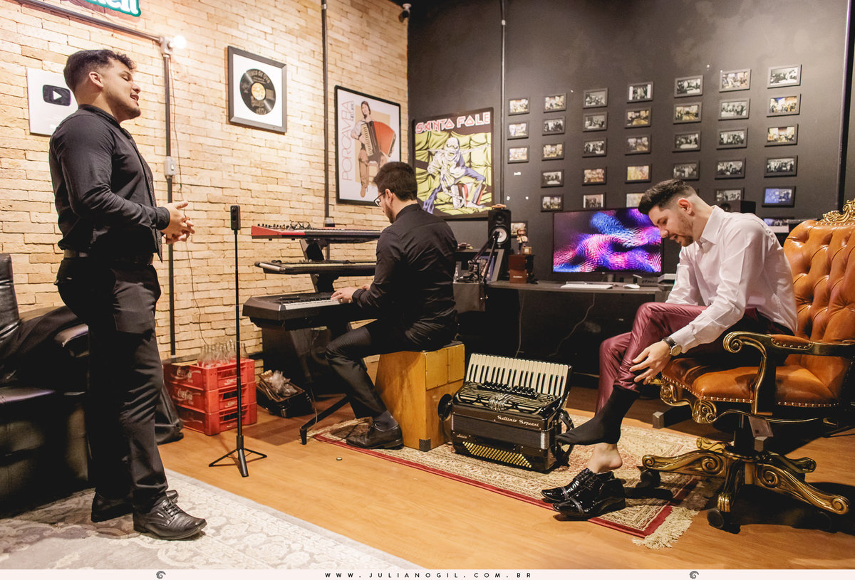 noivo Andriel vestindo os sapatos enquanto está cantando com seu padrinho e outro padrinho tocando teclado durante o making of