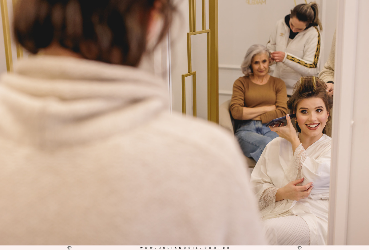 noiva no primeiro plano com celular ao ouvido e ao fundo a sogra da noiva com a penteadista