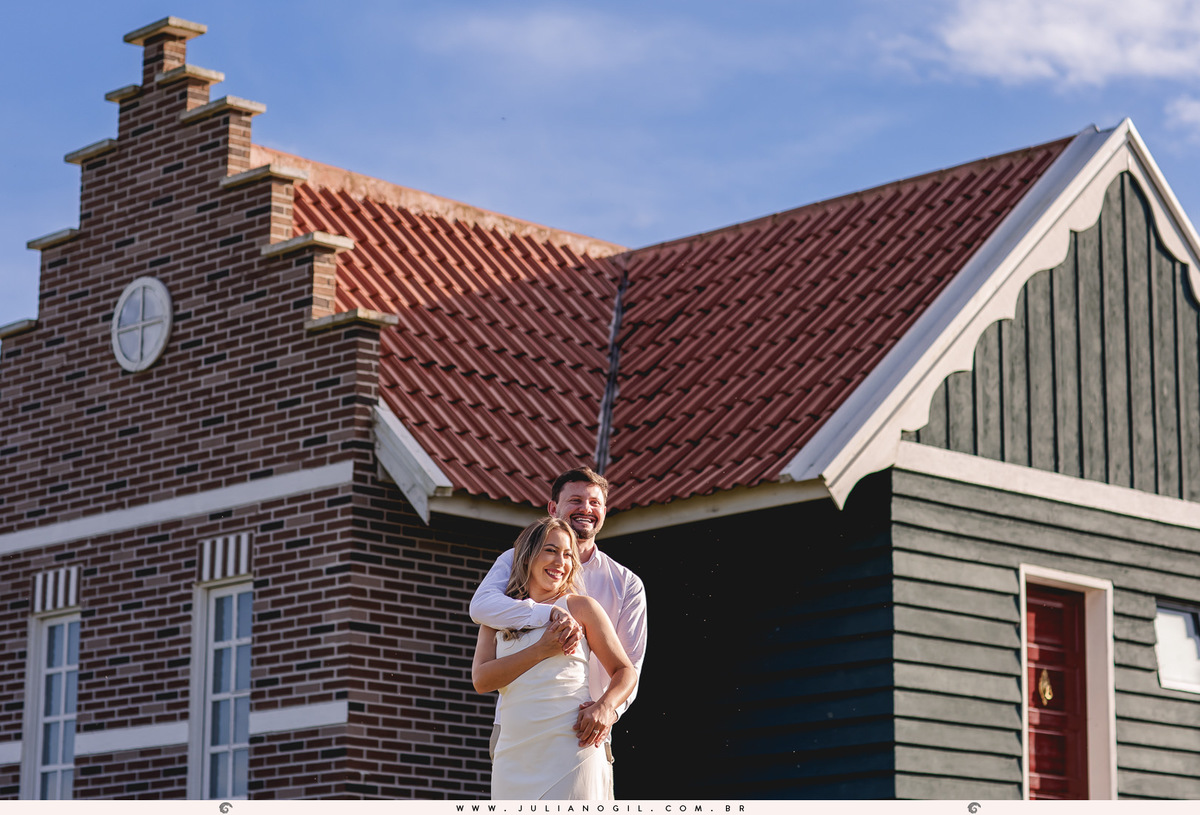 casal sorrindo e se abraçando em frente a uma casa estilo holandesa