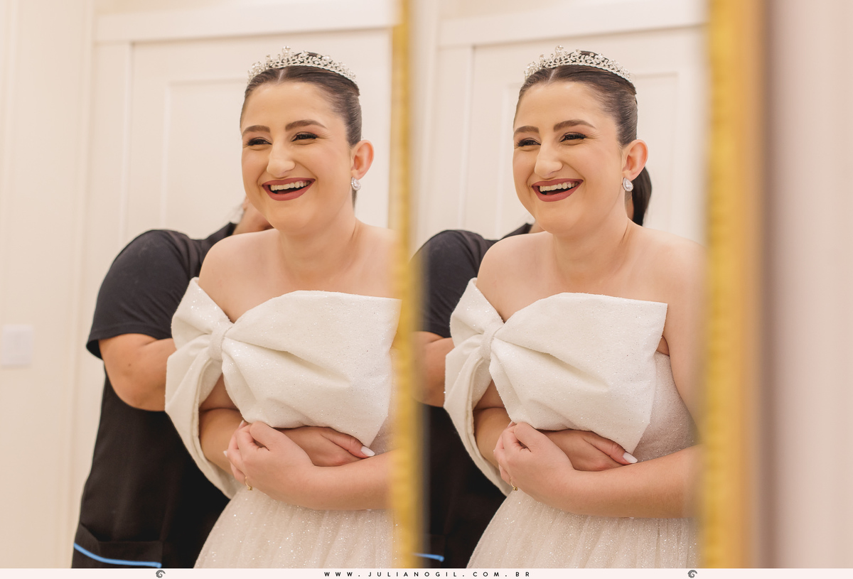 noiva adriele em frente ao espelho sorrindo enquanto recebe a ajuda da penteadista para colocar o seu vestido