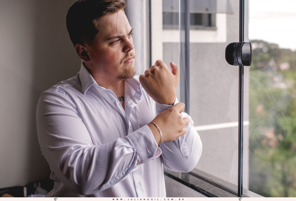 noivo aldo fechando os botões da camisa em frente a uma janela