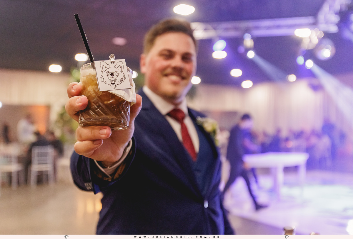 noivo aldo segurando um drink com uma etiqueta com a foto do cachorro do casal colt
