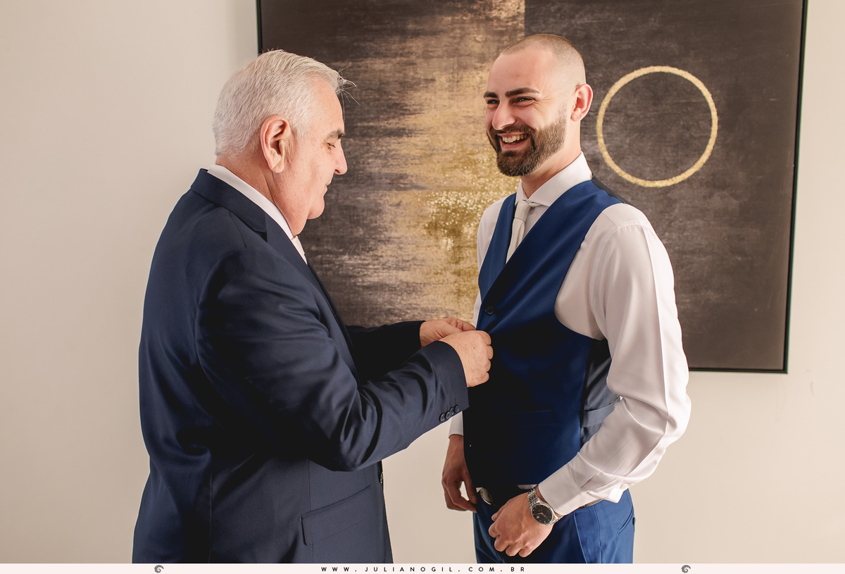 pai do noivo vestindo o colete no filho durante o making of do noivo em casa 