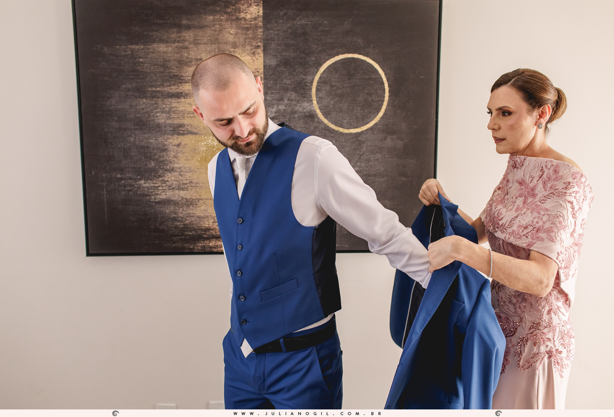 mãe do noivo vestindo o terno no filho durante o making of do noivo em casa 