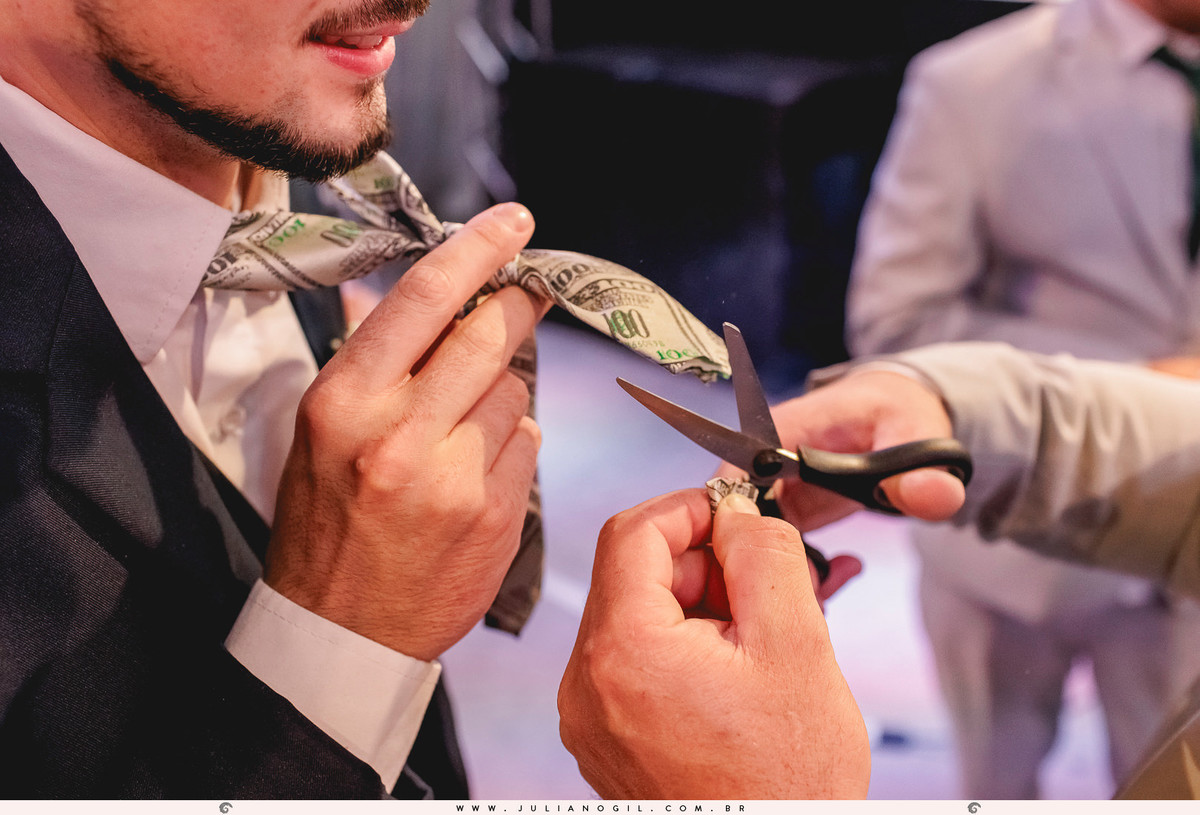 padrinho cortando a gravata do noivo durante a festa de casamento em durante a festa de casamento em Rio Azul, Paraná