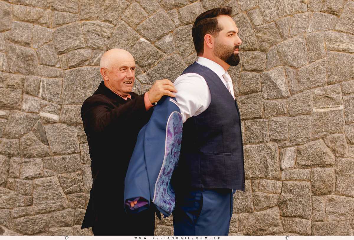 pai do noivo vestindo o filho antes da cerimônia de casamento