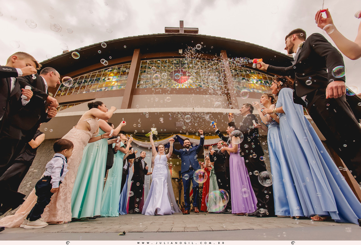 saída dos noivos da igreja com padrinhos jogando bolhas sobre o casal