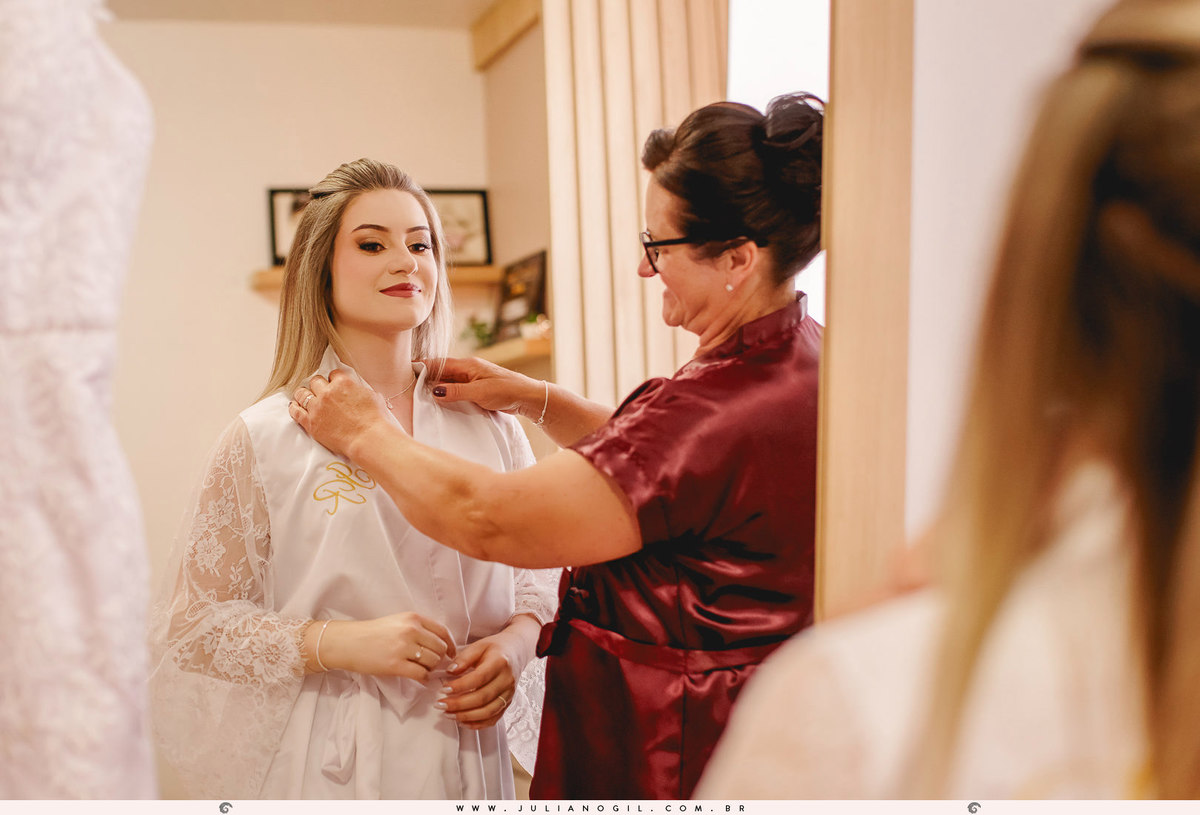 mãe da noiva ajeitando o colocar no pescoço da noiva em frente ao espelho