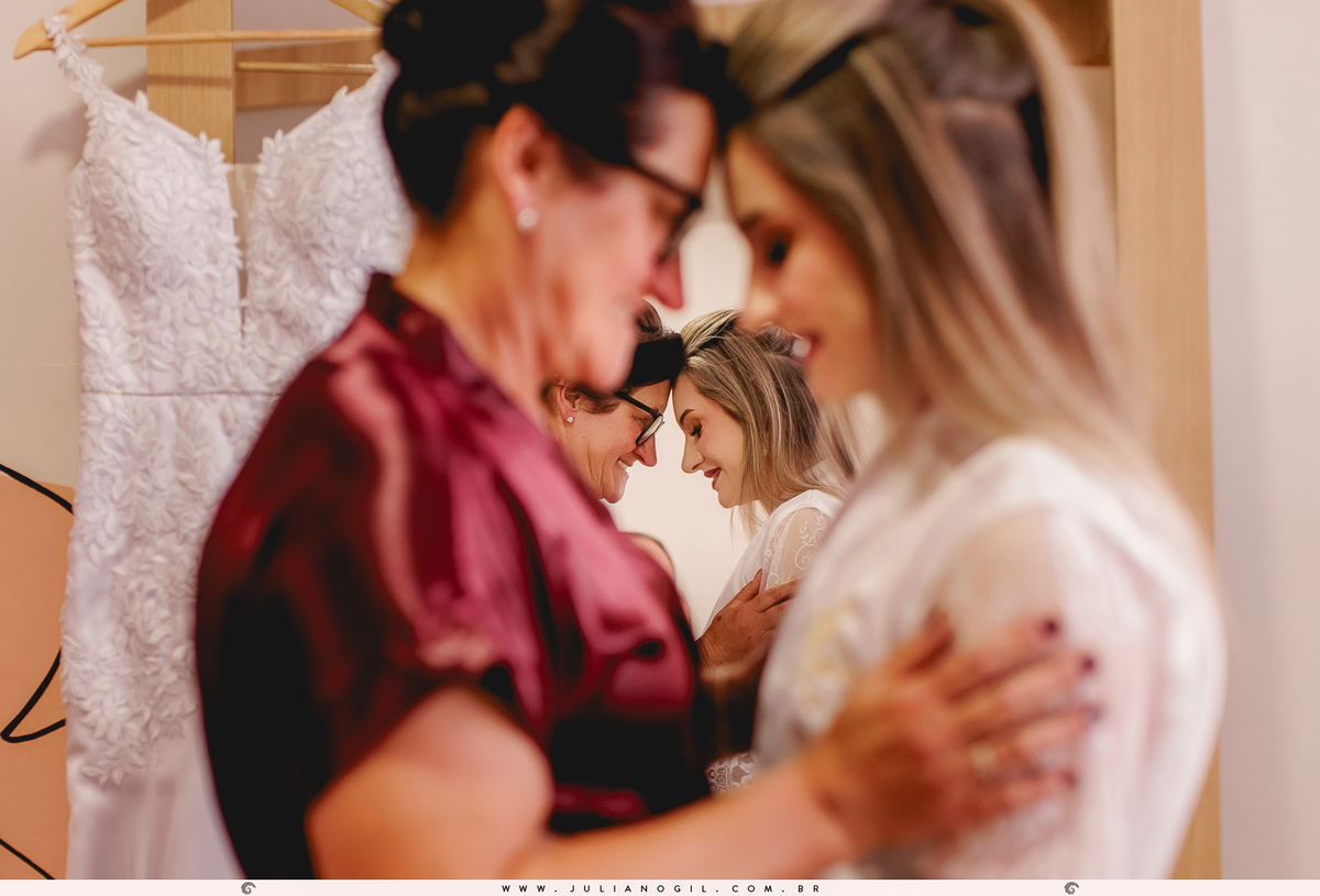 noiva e sua mãe com as testas encostadas em frente ao espelho