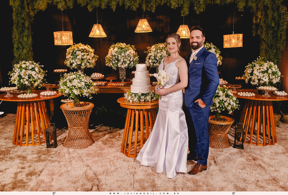 noivos em frente a mesa de doces na festa de casamento