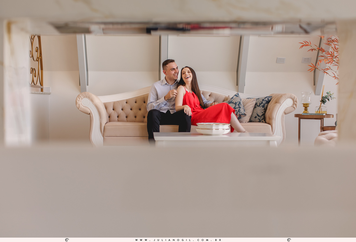 noivos sentados no sofá abraçados, a moldura da foto é feita pelo vão da parede da lareira