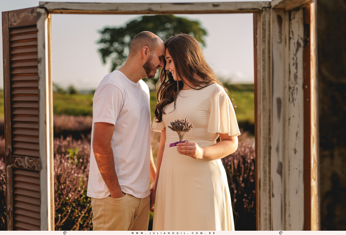 casal com os rostos encostados pela testa, sendo emoldurados por uma janela em meio a uma plantação de manjericão no lavandário dos sonhos em witmarsum no paraná