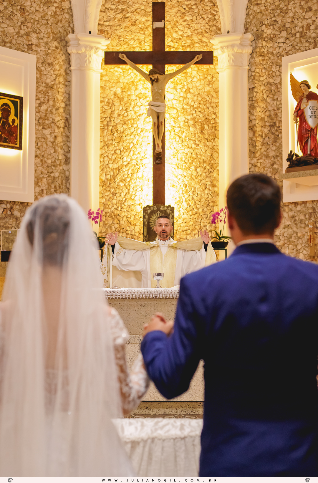 padre fazendo uma oração de braços abertos no altar de frente para os noivos