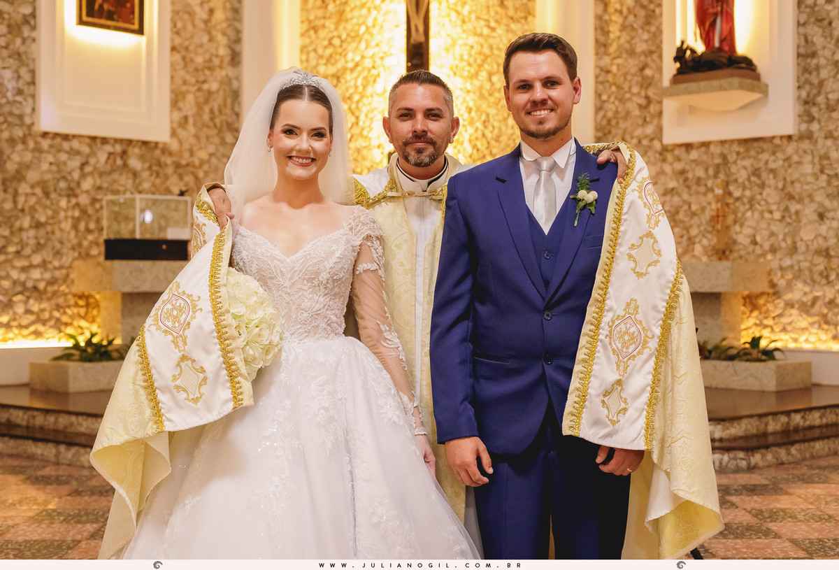 foto posada dos noivos com o padre com a batina sobre o casal