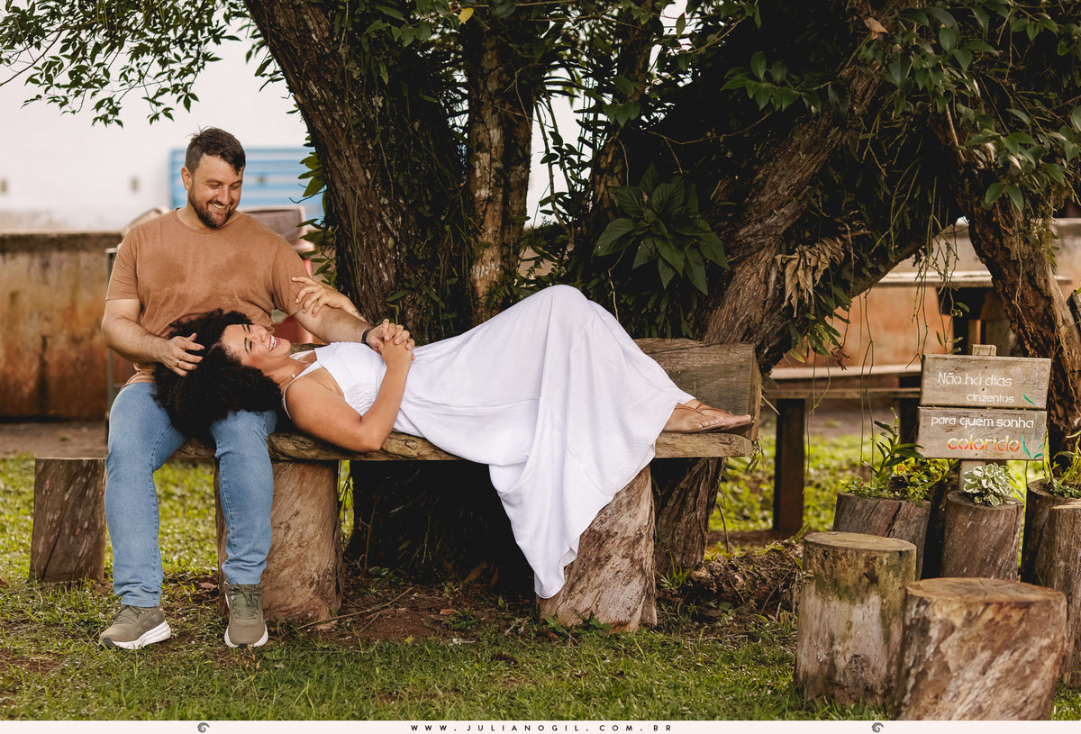 noivo sentado e noiva deitada com a cabeça no colo dele em um banco feito de tocos de árvore