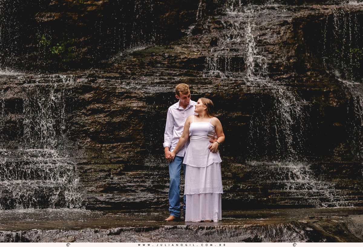 casal em frente a uma cachoeira, sobre as pedras