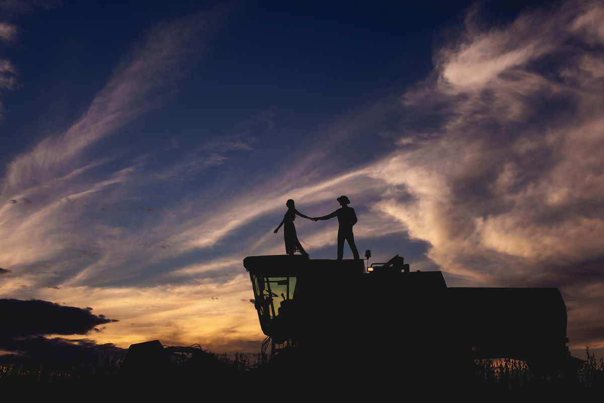 silhueta do casal em cima da colheitadeira sob o pôr do sol