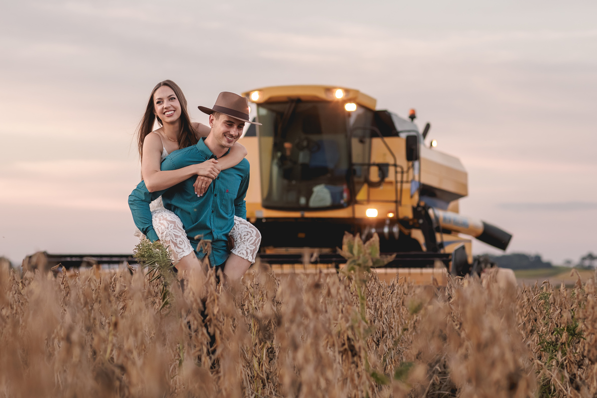 casal caminhando em meio a colheita de trigo, a o fundo a colheitadeira