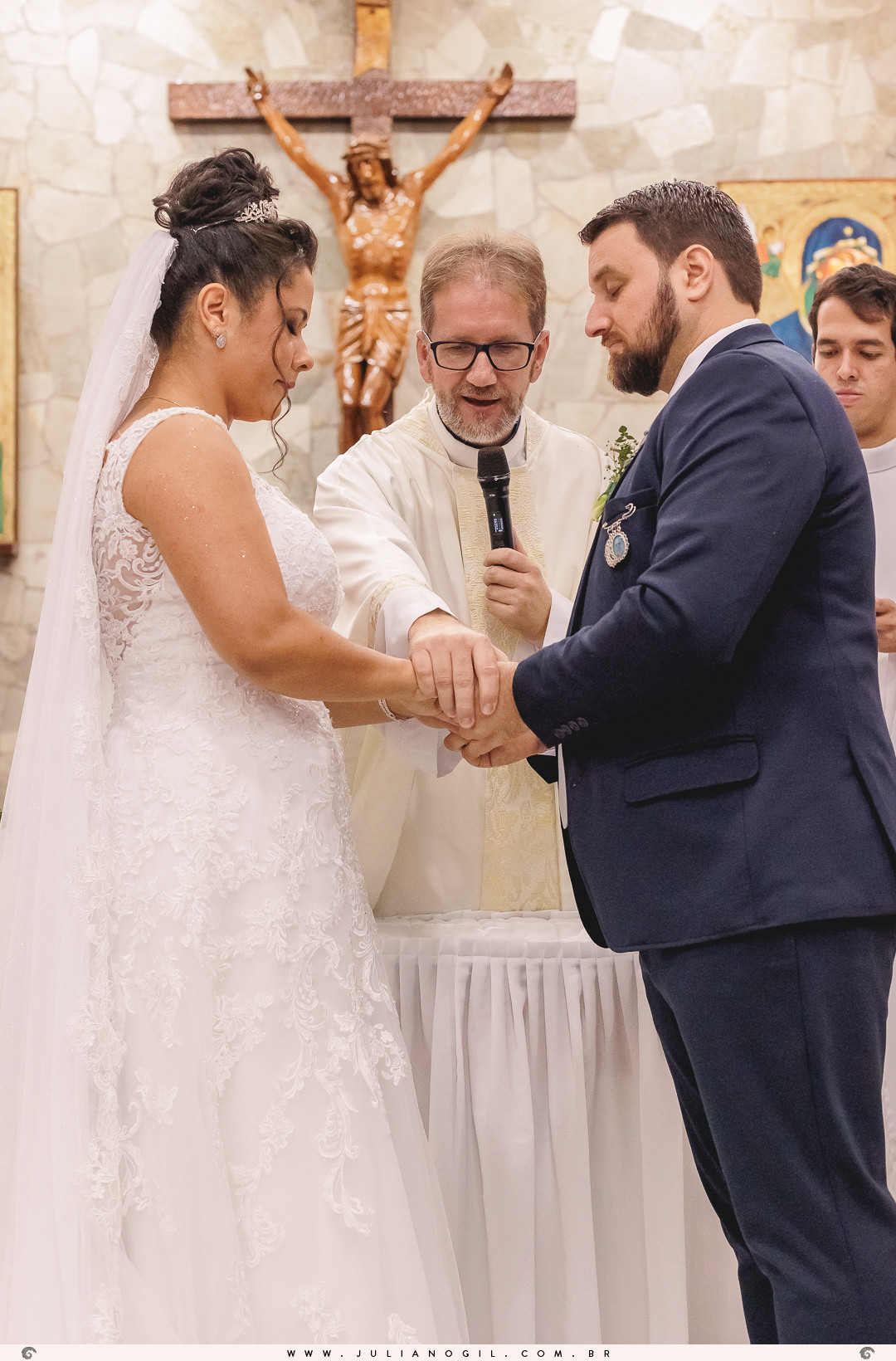 padre abençoando a união do casal segurando as mãos dos noivos