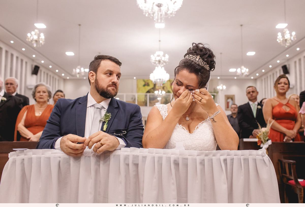 noiva emocionada limparndo o rosto com guardanapo e noivo admirando a noiva
