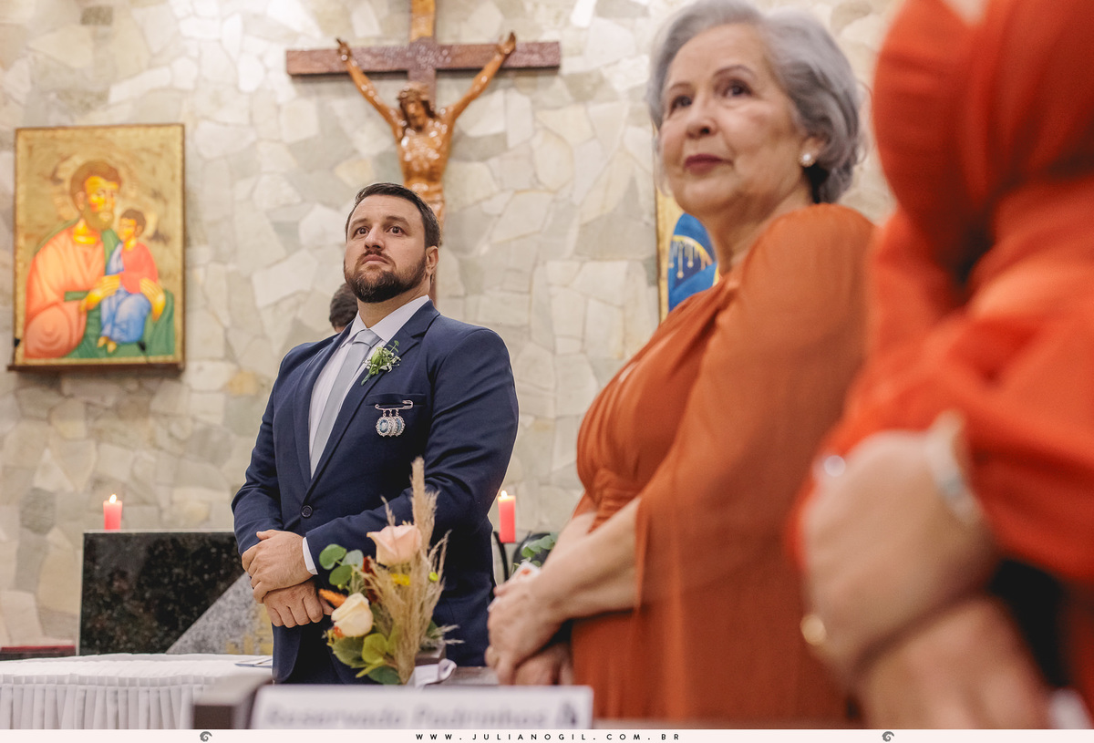 noivo aguardando no altar sendo visto ao fundo, e detalhes das madrinhas em primeiro plano