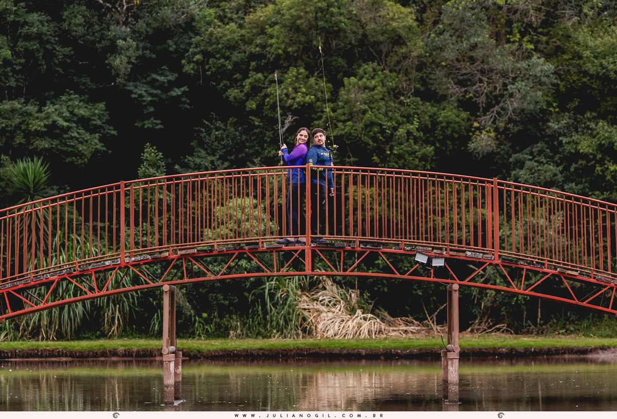casal vestido com roupas de pesca segurando varas de pesca sobre uma ponte