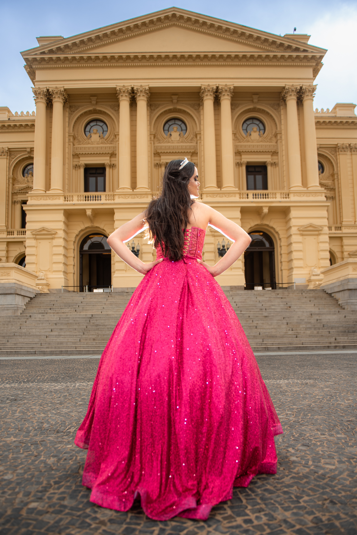 O vestido de gala vermelho contrasta com o cenário clássico do Museu, criando uma composição fotográfica poderosa.