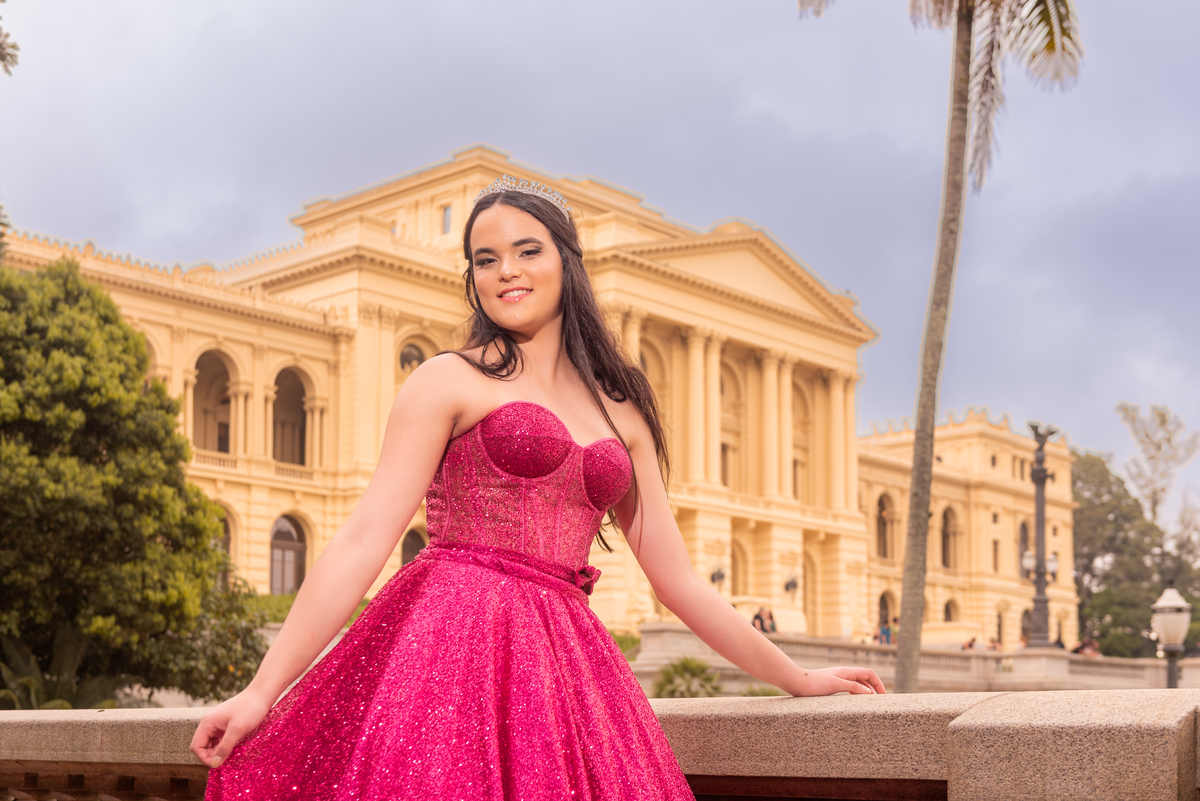 Em um cenário histórico, a debutante caminha como uma rainha, com seu vestido de gala deixando uma marca de elegância.