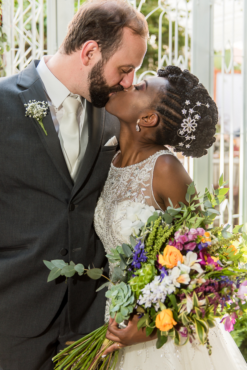 casal se beijando com o buquê na mão da noiva negra