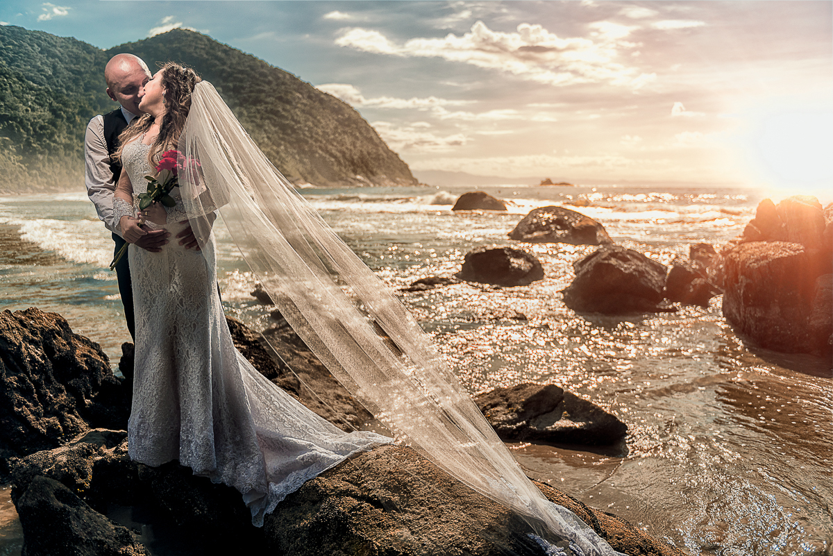 fotografia dos noivos na beira da praia ao por do sol.