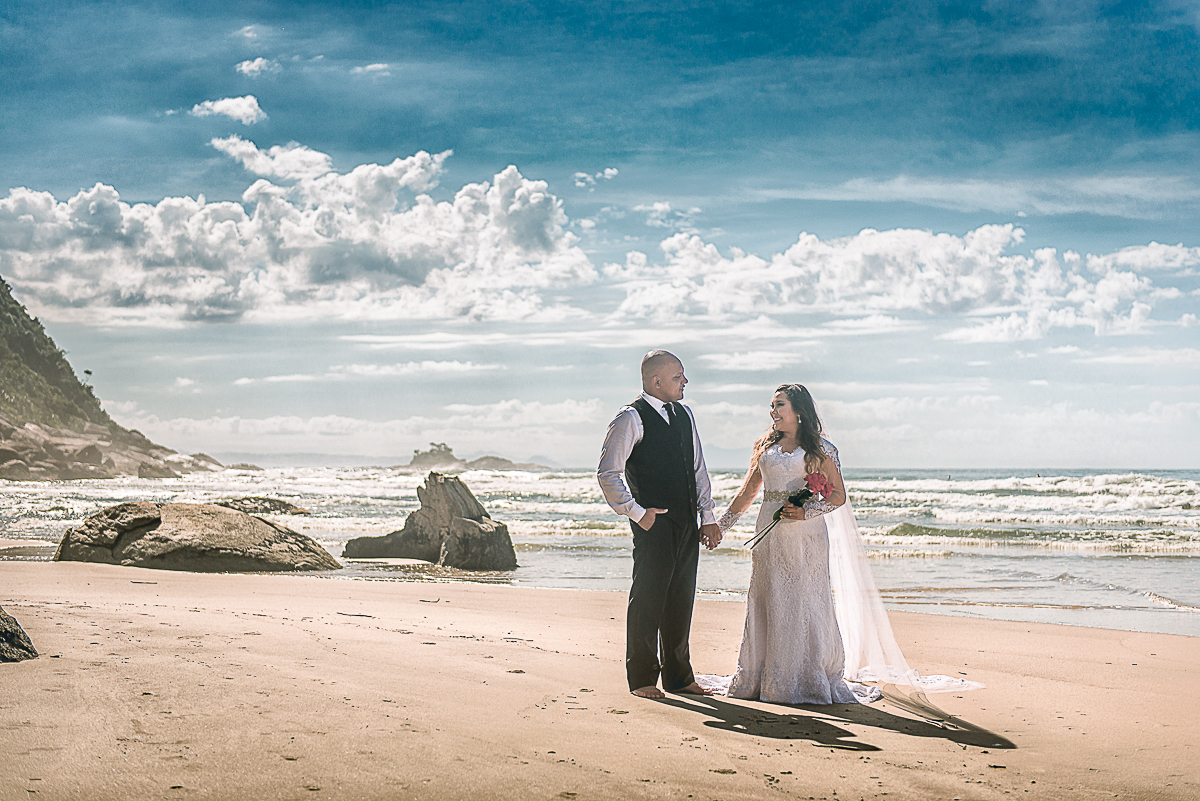 noivos de mãos dadas na praia com um lindo céu azul.