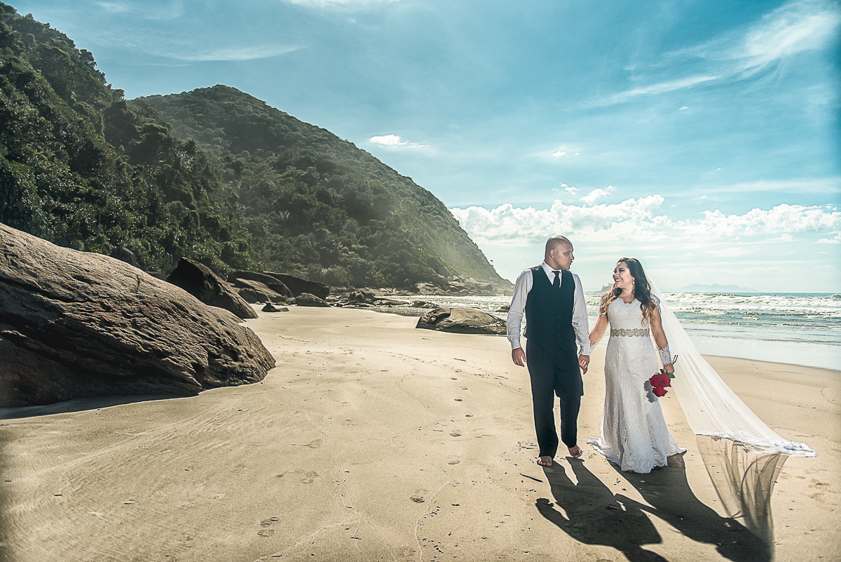 Noivos caminhando pela praia do Guarujá em ensaio trash the dress.
