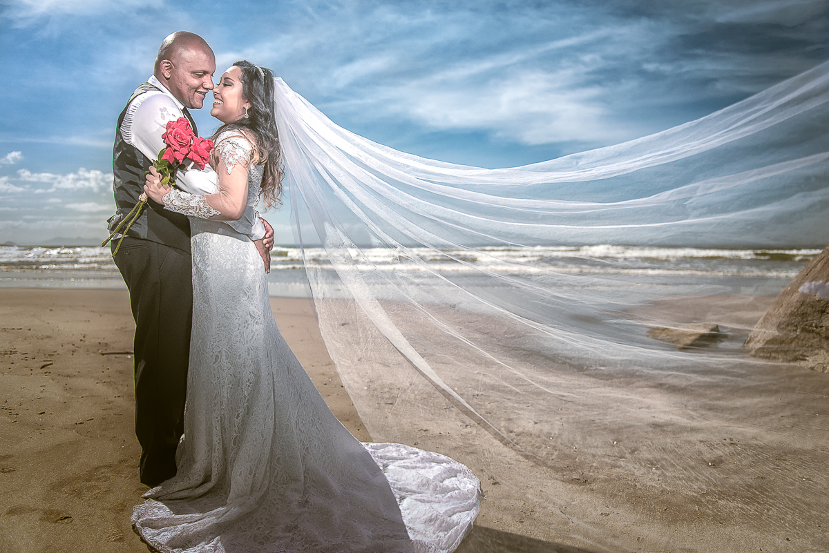 Noivos vestidos véu e grinalda na praia para ensaio fotográfico.