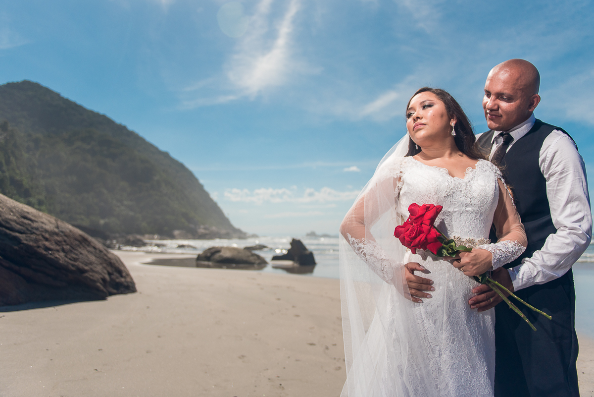 Noivo e noiva e buquê de rosas para ensaio na praia.