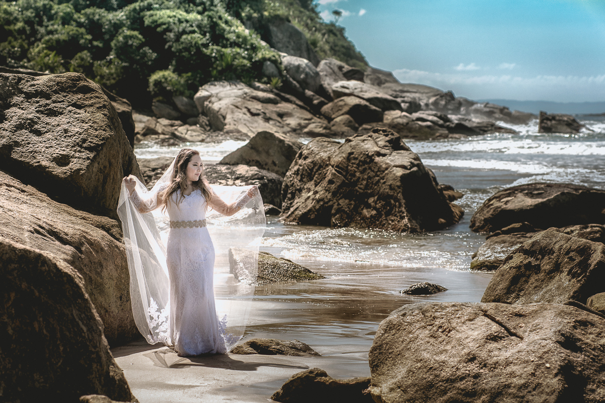Nas pedras da praia a noiva caminha para sessão de fotos.