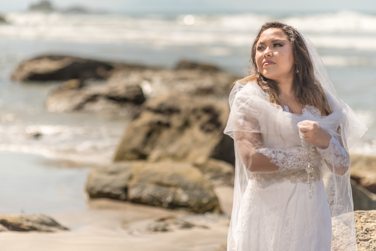 Noiva envolvida pelo seu véu nas areias da praia.